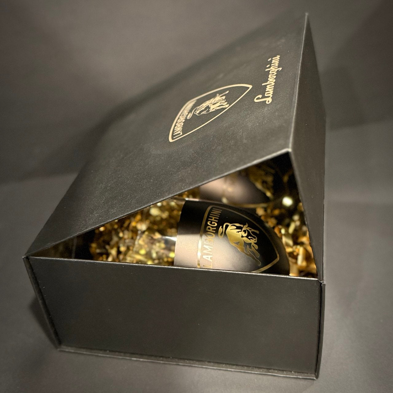 Partially open black luxury gift box revealing bull-inspired black and gold glasses with gold decorative filler