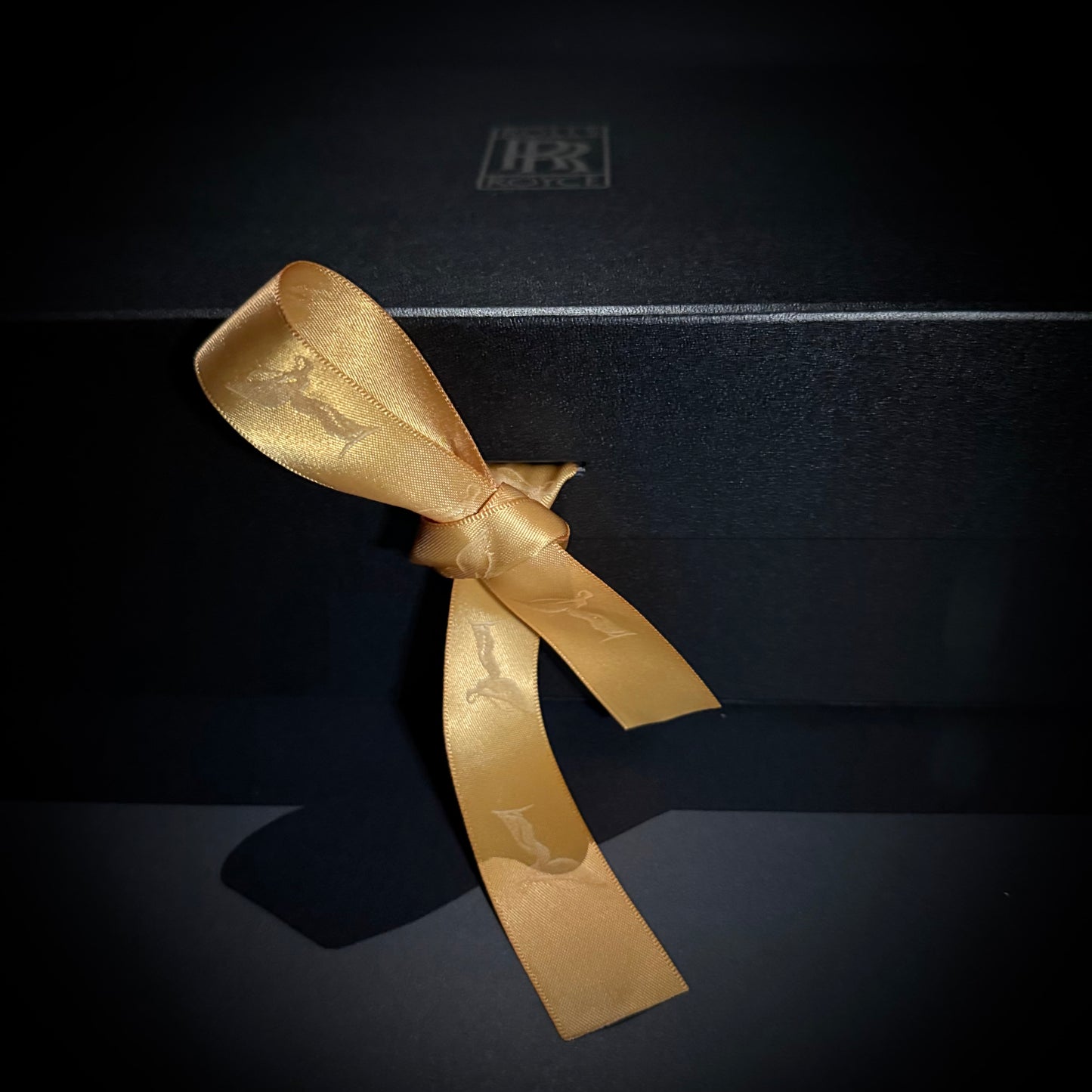 Close-up of a gold ribbon tied on a matte black gift box.