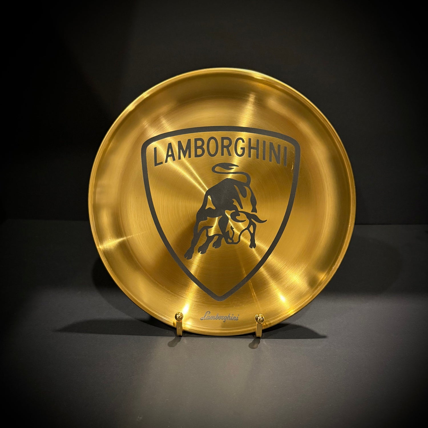 Golden stainless steel display plate with engraved bull-inspired crest on a display stand.