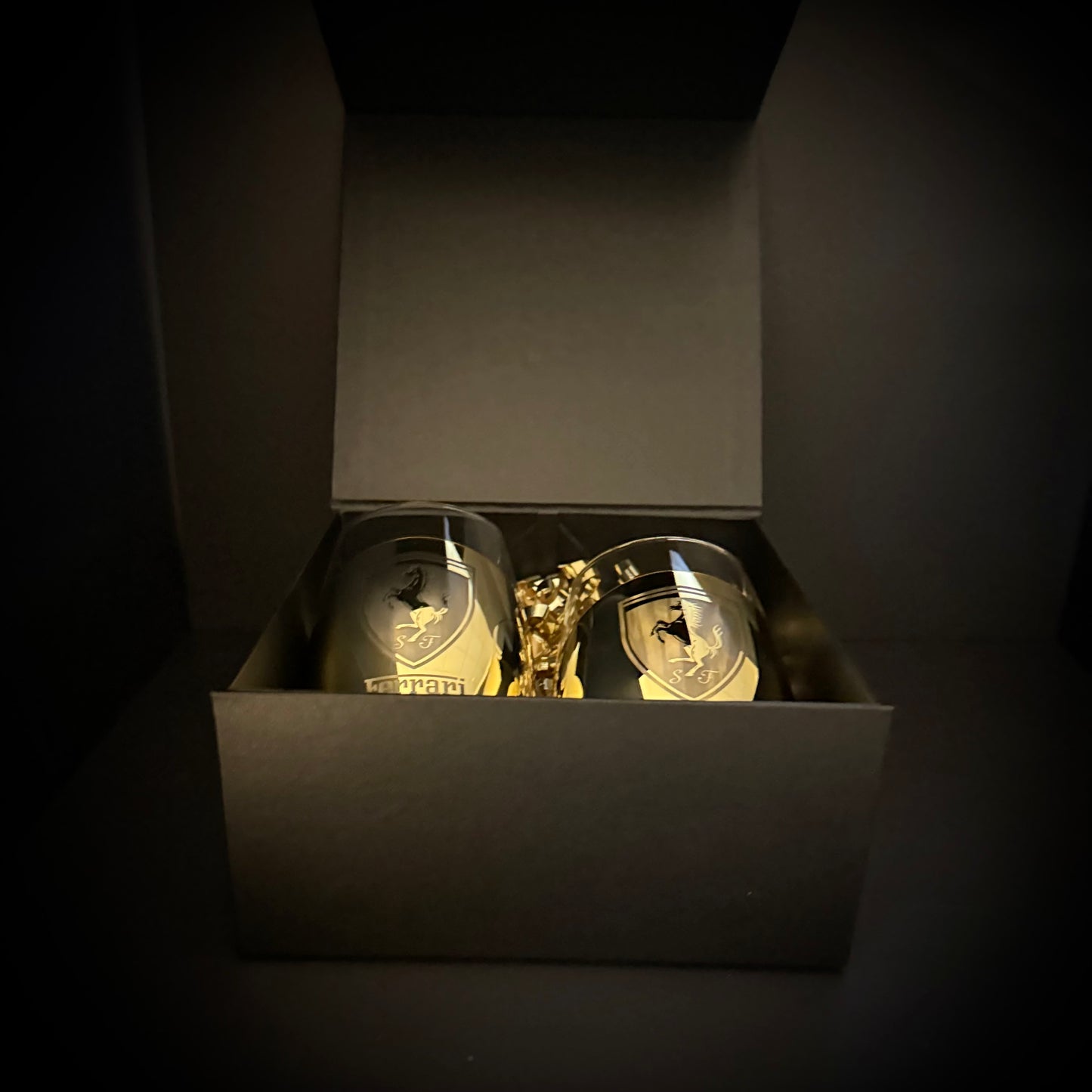 Two gold cups with a Ferrari logo in a black box on a dark background