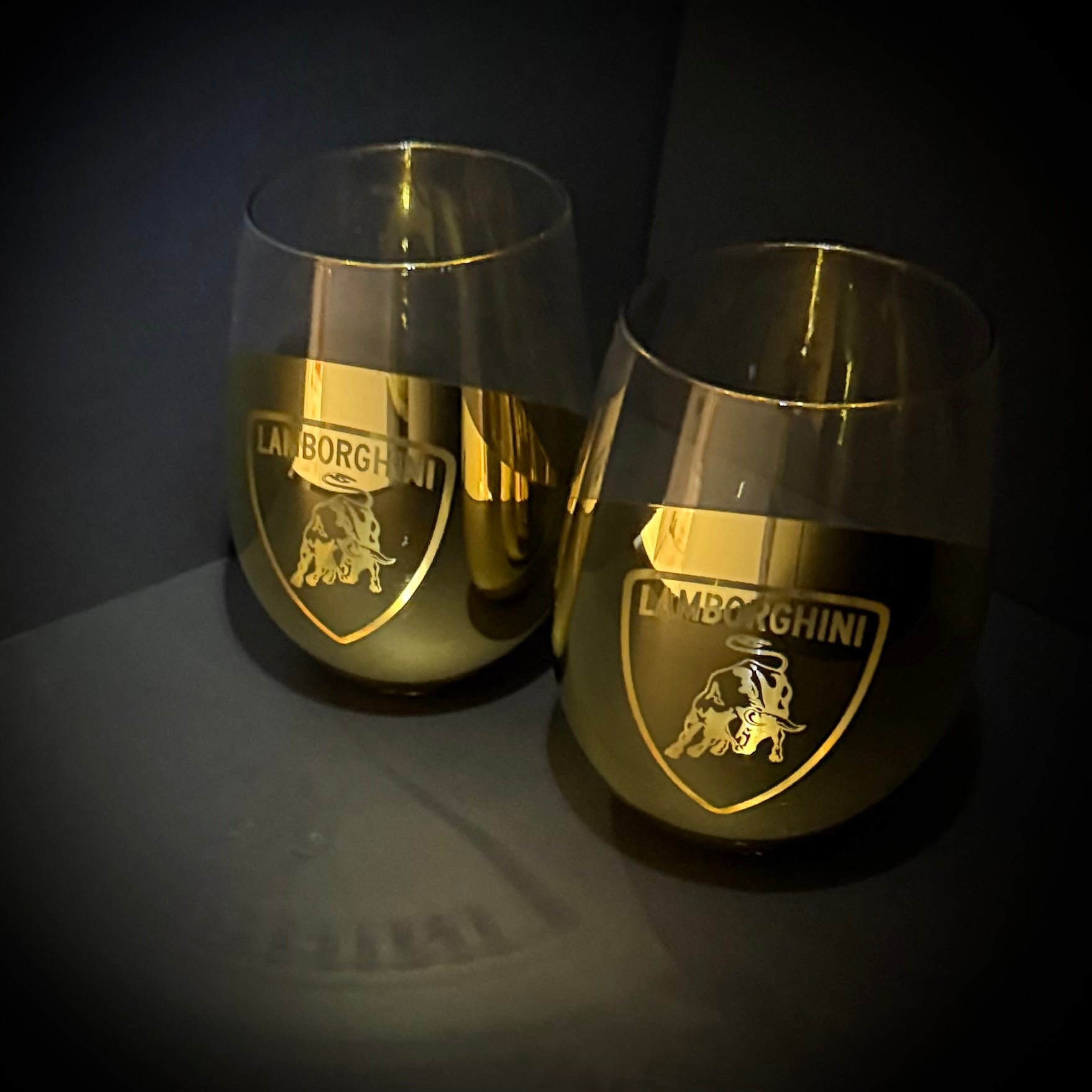 Two gold Lamborghini-branded wine glasses on a dark background