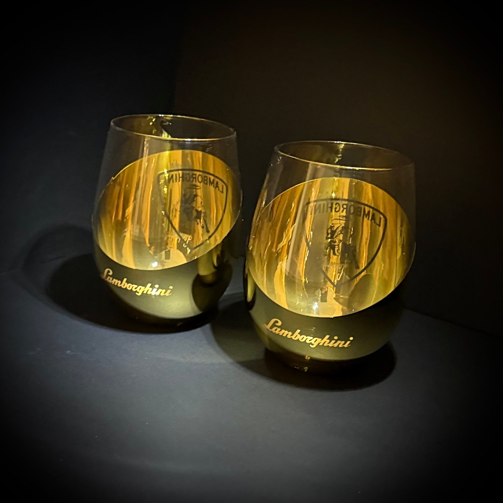 Two gold Lamborghini-branded glasses on a dark background