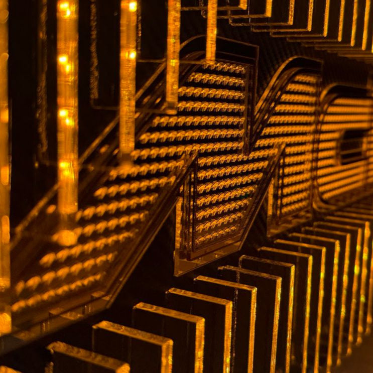 Close-up of a McLaren-inspired acrylic sculpture showing layered transparent fins, micro-logo detailing, and carbon-fiber texture illuminated with orange LED lighting.