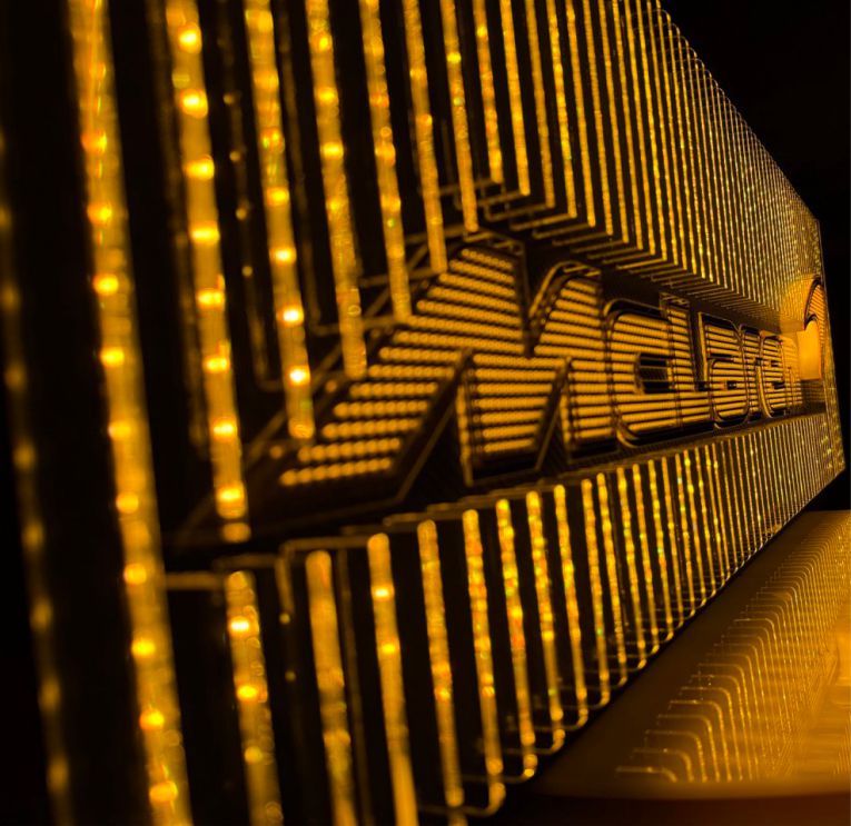 Detailed view of a McLaren-inspired acrylic artwork featuring reflective fins, micro-logo texture, carbon-fiber backing, and soft orange LED illumination.