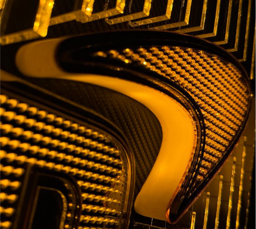 Clean view of the McLaren-inspired acrylic wall piece showcasing layered fins, carbon-fiber base, micro-logo texture, and soft orange LED lighting.