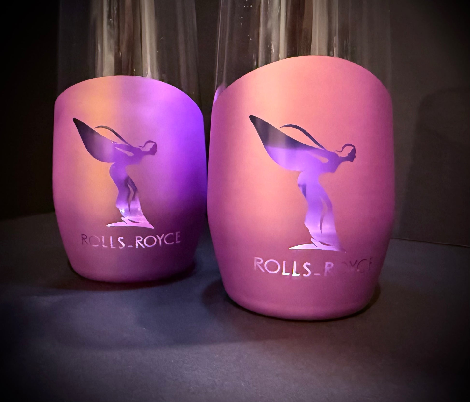 Close-up of two matte purple luxury drinkware glasses with a spirit-inspired silhouette design on a dark background.