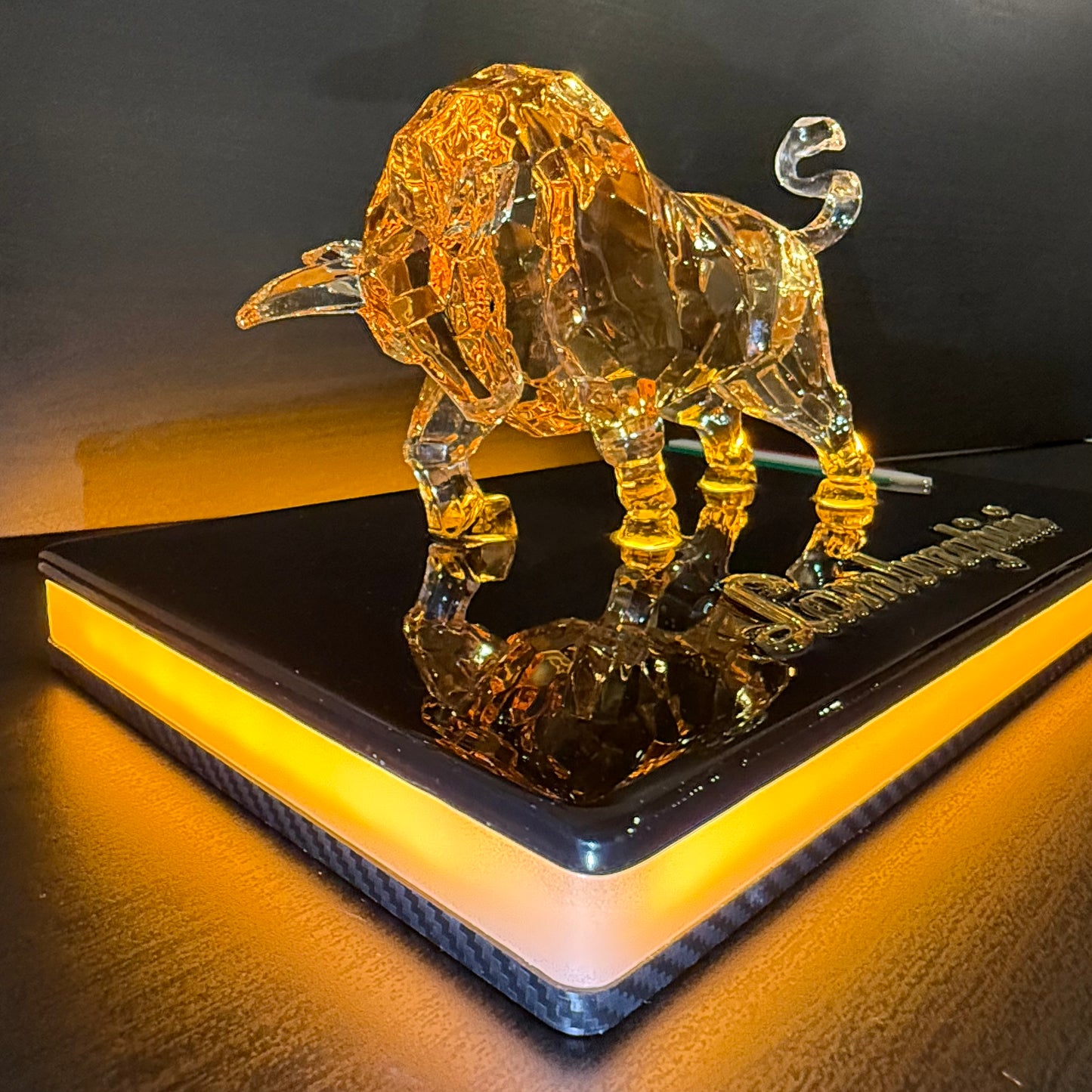 Illuminated golden bull sculpture on a black acrylic base with warm LED lighting, close-up front view.