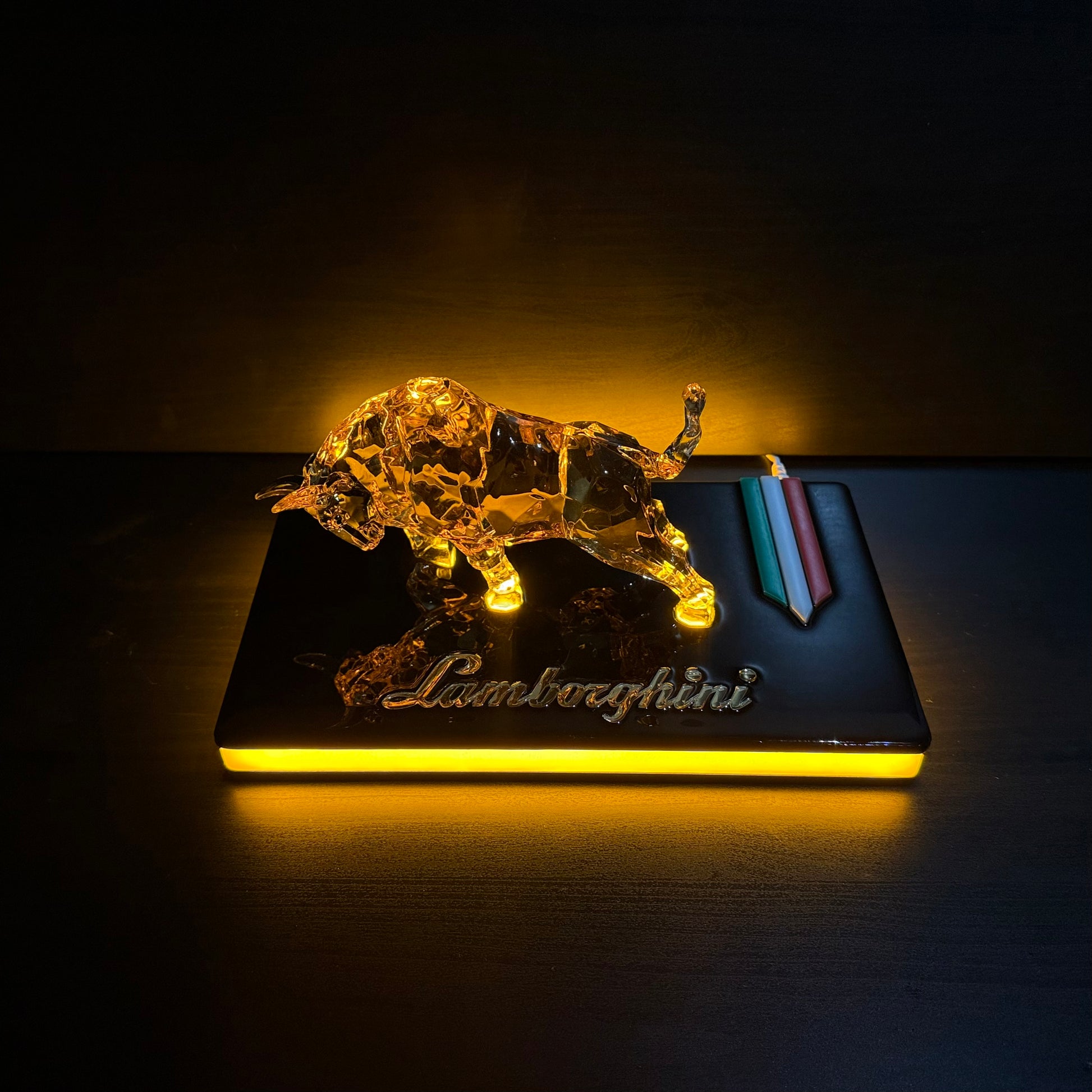 Golden bull figurine glowing under warm light on a glossy black base, angled side view.