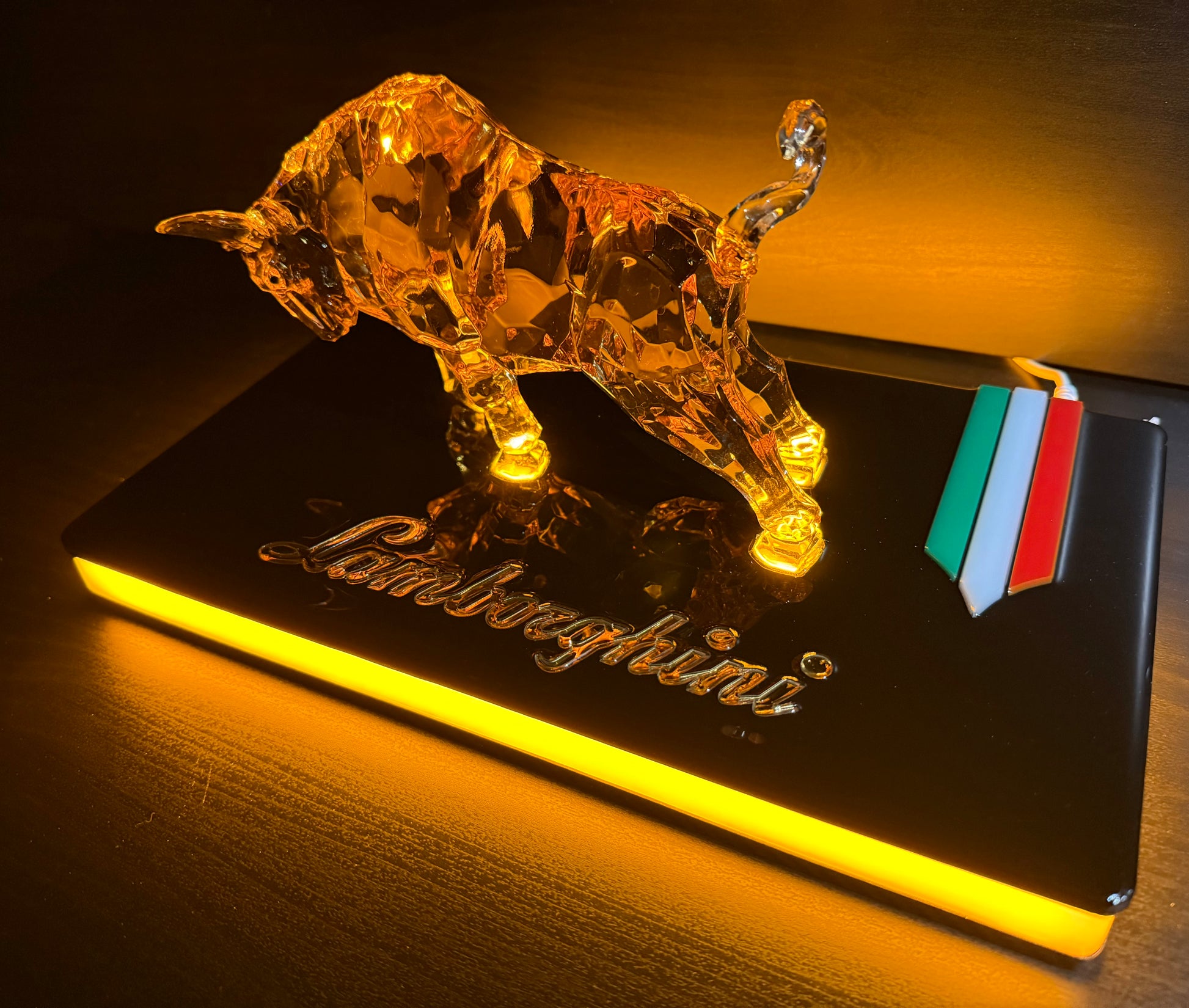 Bull sculpture with golden LED glow displayed on a dark base with colorful reflections on the right side.