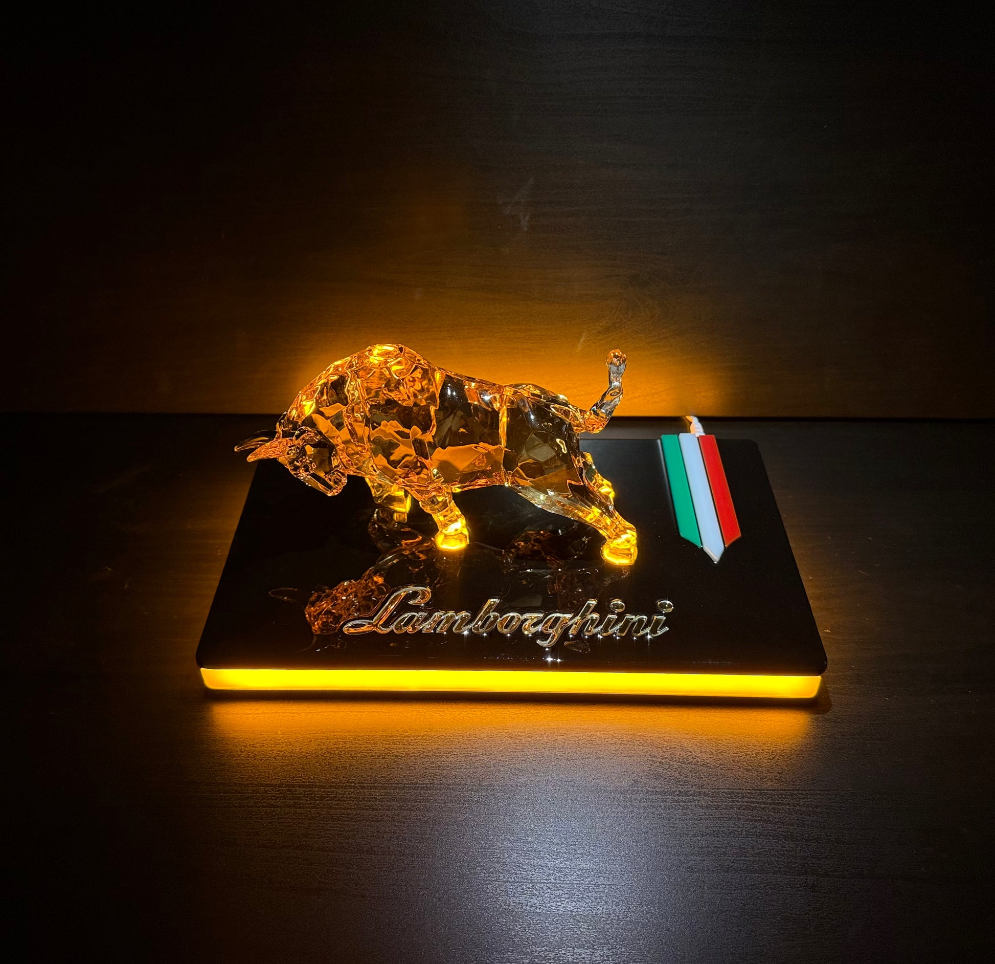 Wide shot of the glowing golden bull sculpture centered on a glossy black platform with warm ambient lighting.