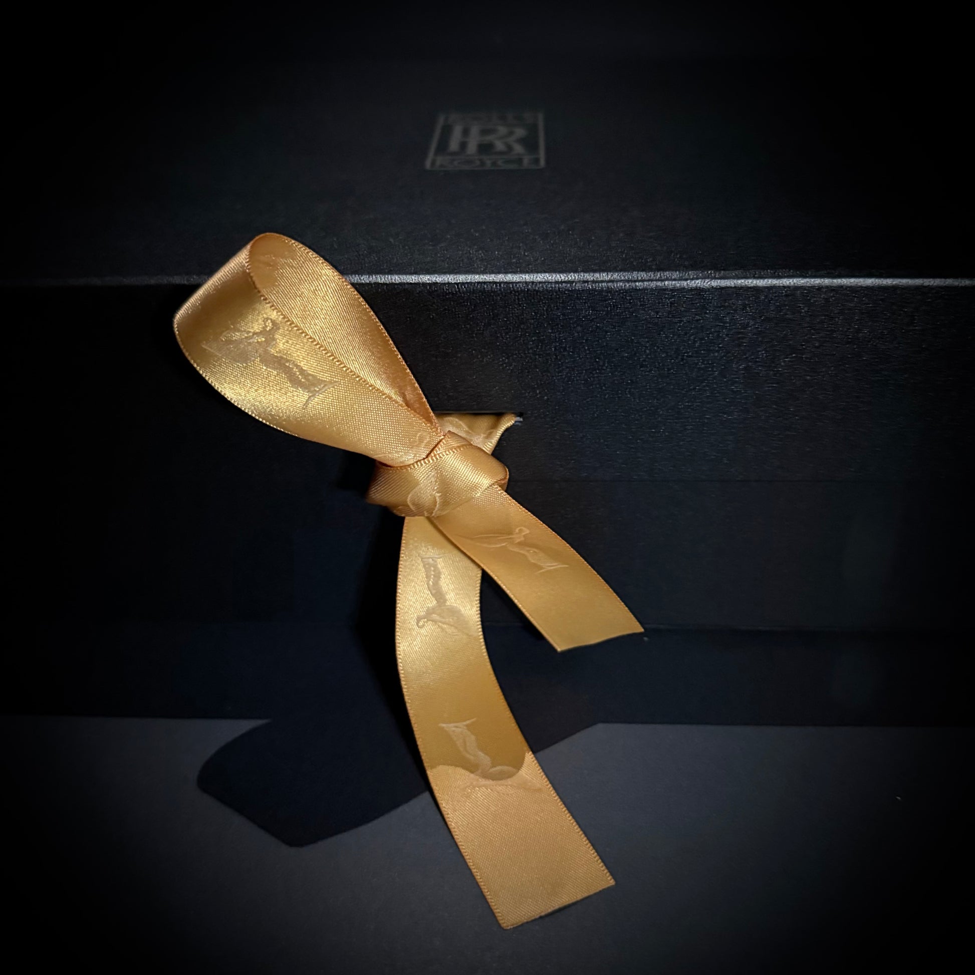 Close-up of a gold ribbon tied on a matte black gift box.